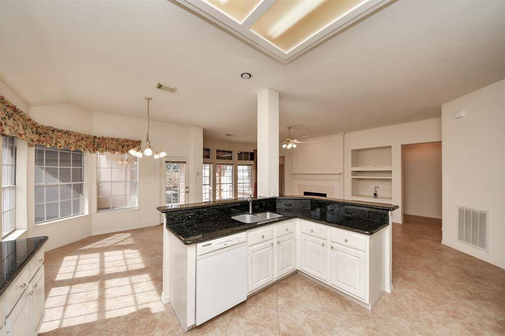 Bright and spacious open-concept kitchen and living area with large windows, a central island with dark countertops, and light tile flooring. The living room features built-in shelving and a cozy fireplace.