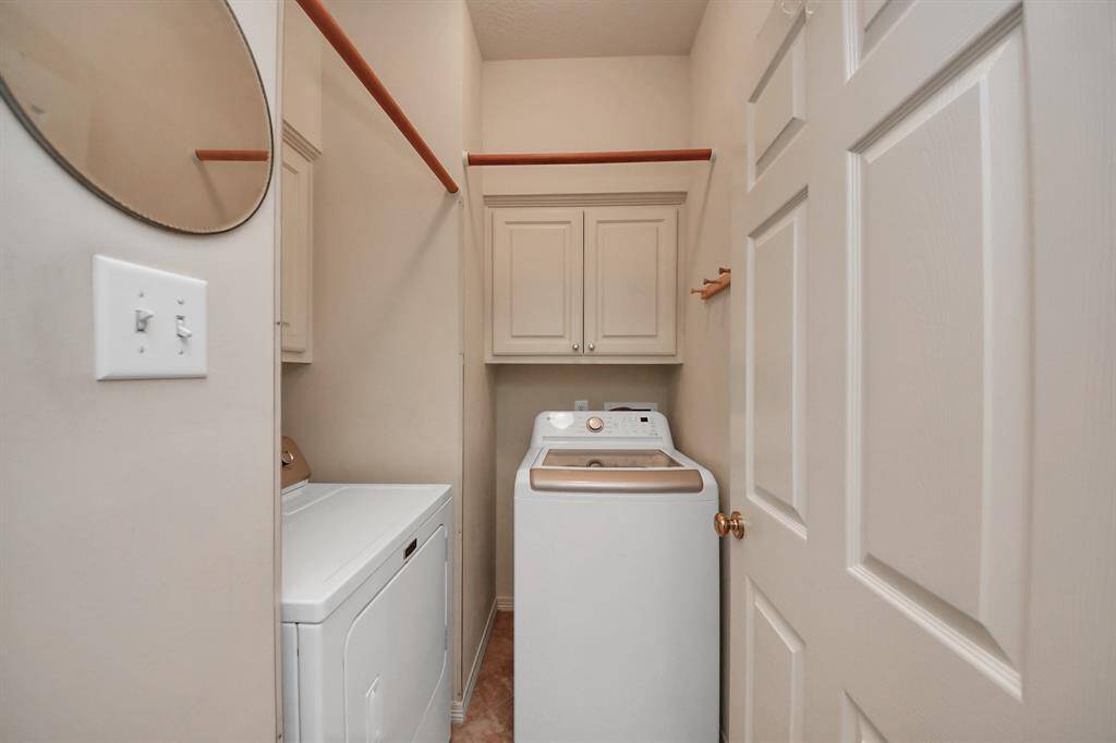 Compact laundry room with a washer and dryer, overhead cabinets for storage, and neutral-colored walls.