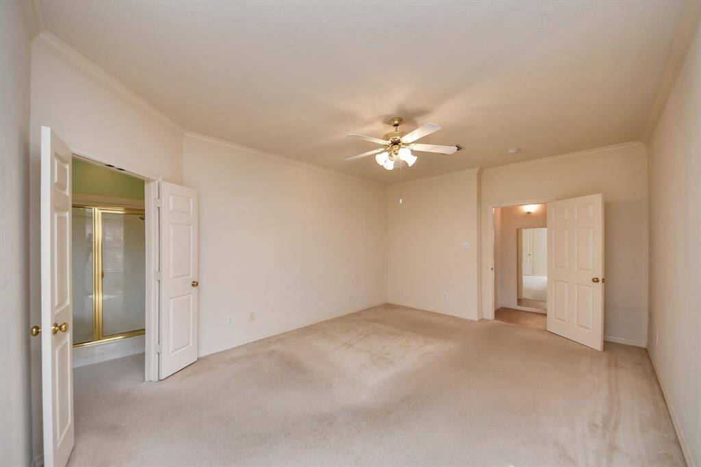 Bright, spacious primary bedroom with neutral walls and carpet, featuring a ceiling fan. It includes an en-suite bathroom with double doors and a walk-in closet for added convenience.