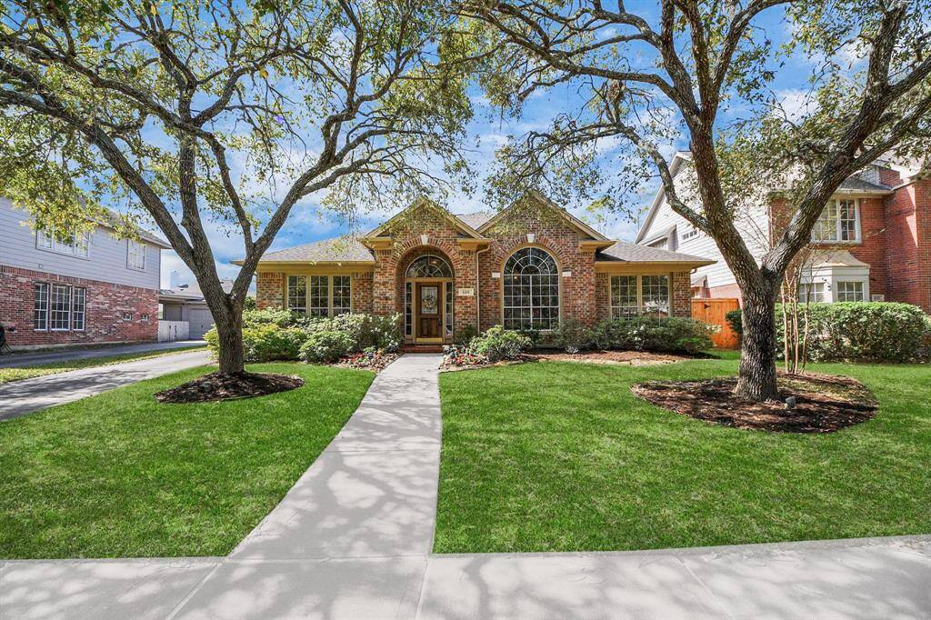 Charming brick home with a welcoming arched entrance, surrounded by lush greenery and mature trees. Features a well-maintained front yard with a central walkway, offering excellent curb appeal in a serene neighborhood setting.