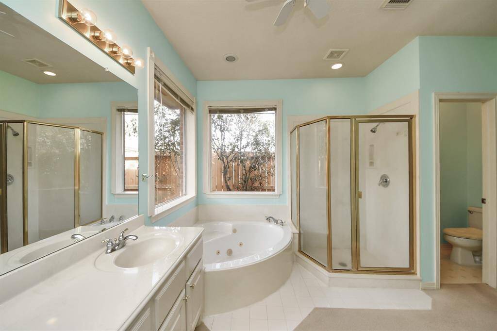 Bright and spacious bathroom featuring a large corner bathtub, separate glass-enclosed shower, dual sinks, and ample natural light from the window.