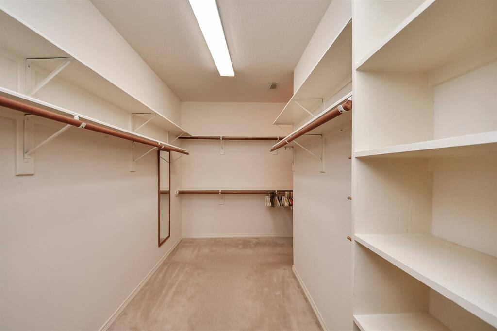 This photo showcases a spacious primary walk-in closet with ample shelving and hanging space, featuring neutral walls and lighting, ideal for organized storage.