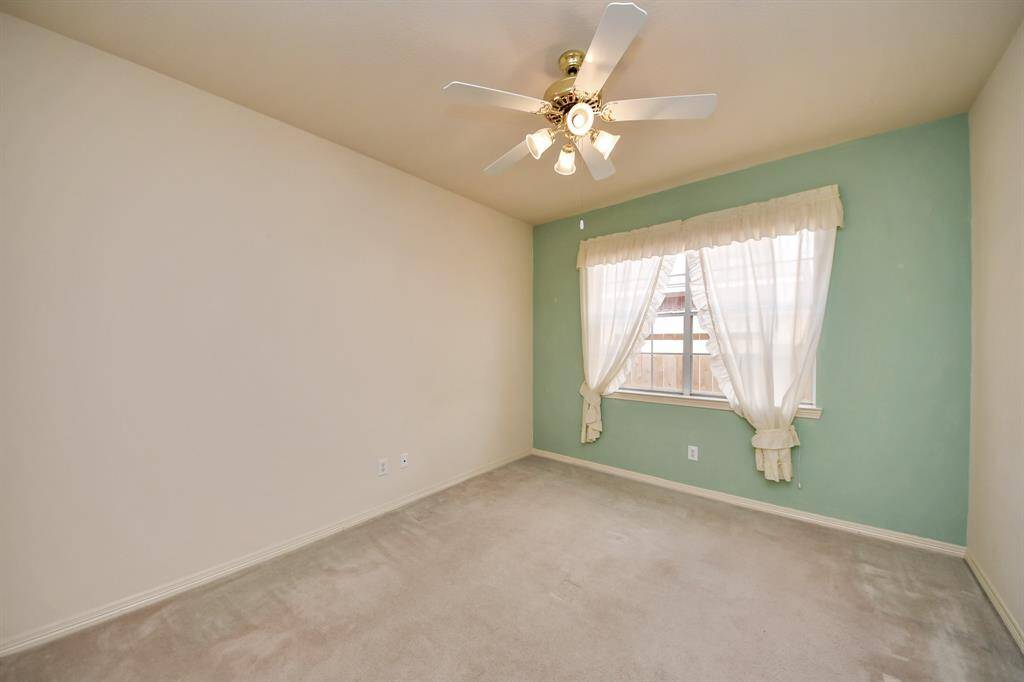 This cozy room features a neutral carpet, light green accent wall, and a window with sheer curtains, providing ample natural light. A ceiling fan adds comfort and functionality.