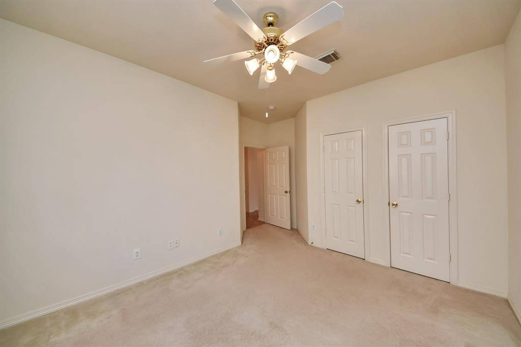This photo shows a bright, neutral-toned bedroom with carpet flooring and a ceiling fan. It features two closets with white doors and appears to be a cozy bedroom or office space.