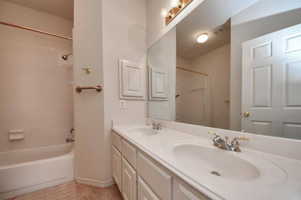 This second bathroom features a double sink vanity with ample counter space, a large mirror, and a shower-tub combo. Neutral tones and overhead lighting create a bright, welcoming atmosphere.