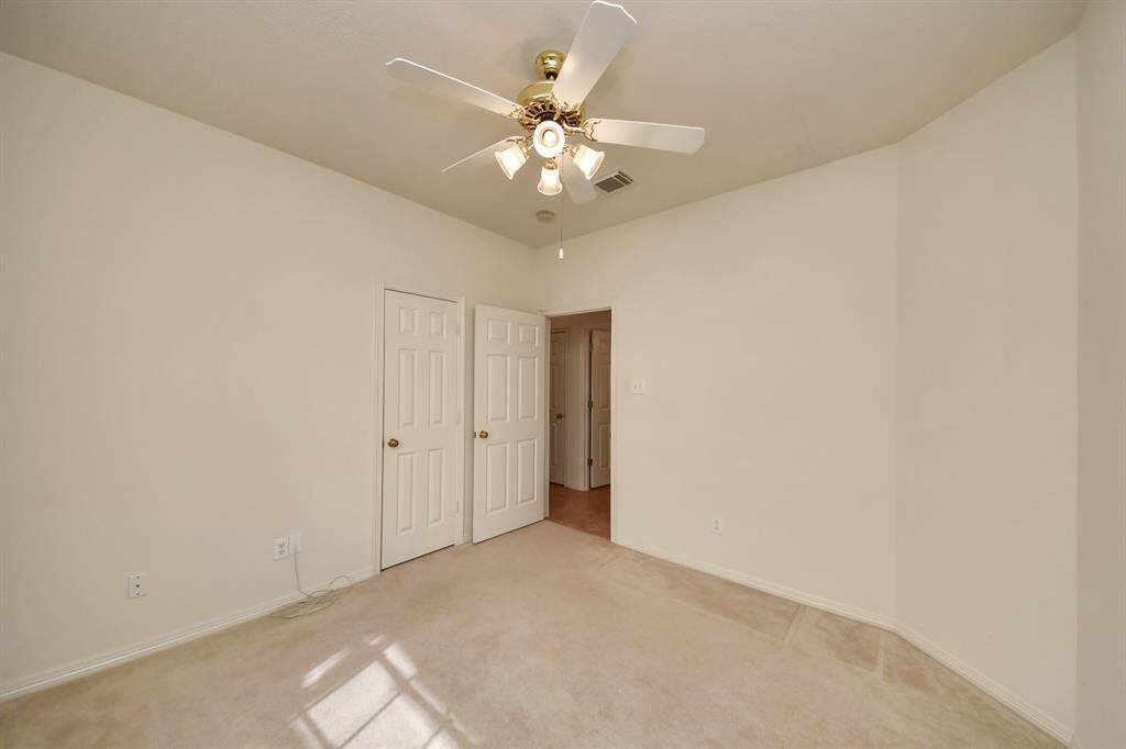 This is a bright, neutral-toned bedroom featuring a ceiling fan with lights. It has carpeted flooring and two doors leading to additional spaces, ideal for a bedroom or office.