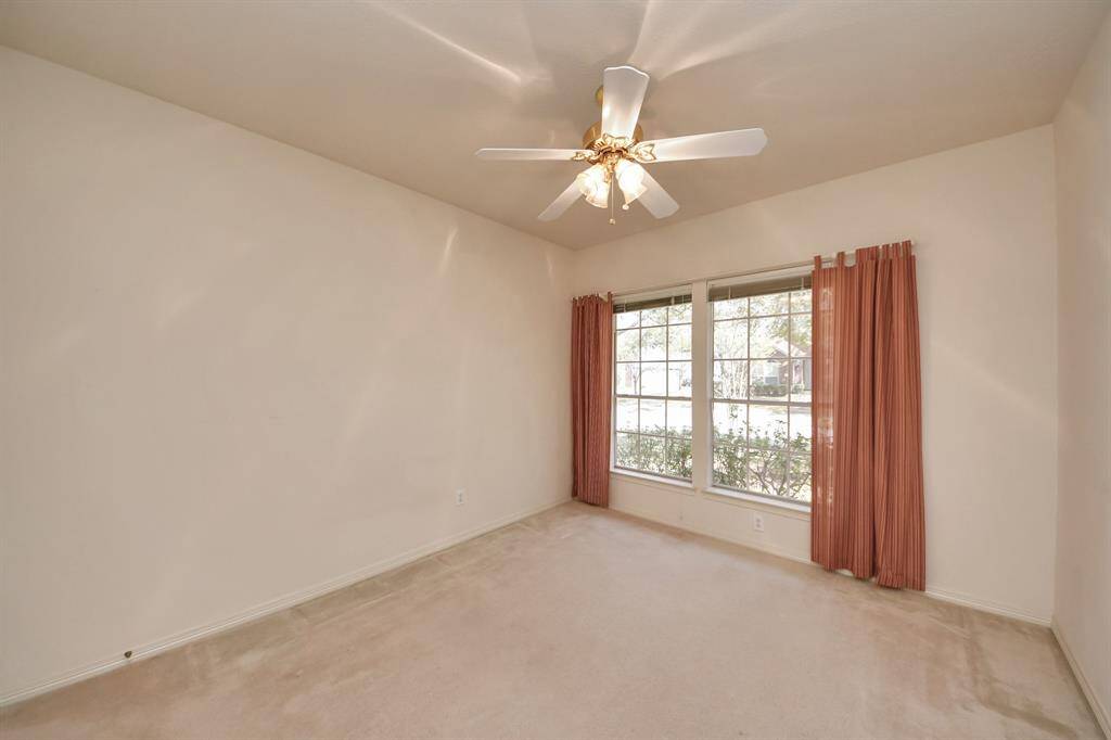 This bedroom features neutral walls and carpeting, a ceiling fan, and large windows, offering ample natural light and a cozy atmosphere.