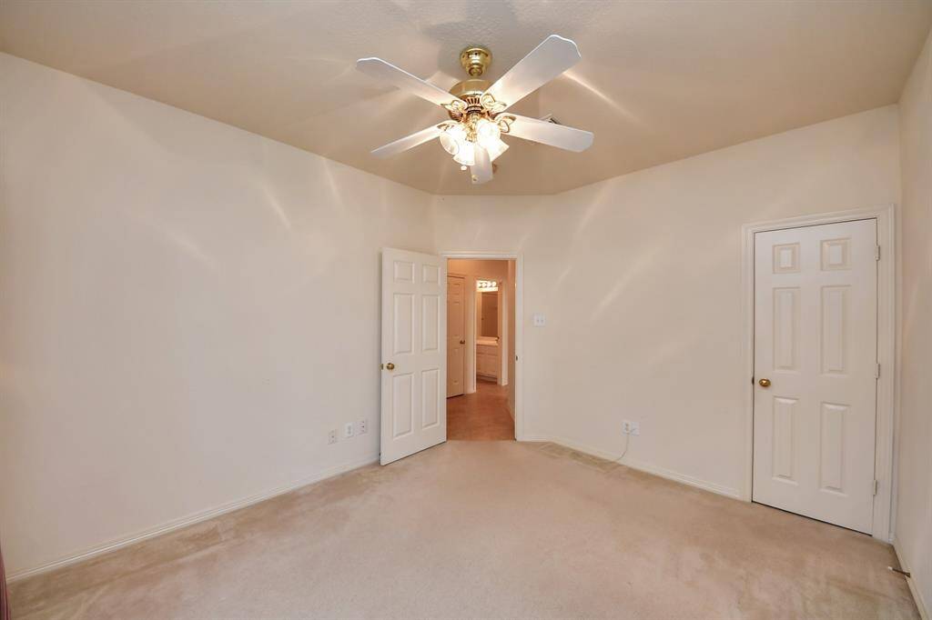 This is a cozy bedroom with neutral walls and carpet, featuring a ceiling fan for comfort. It includes two doors, one leading to a hallway with a glimpse of a bathroom. Perfect for a bedroom or home office.