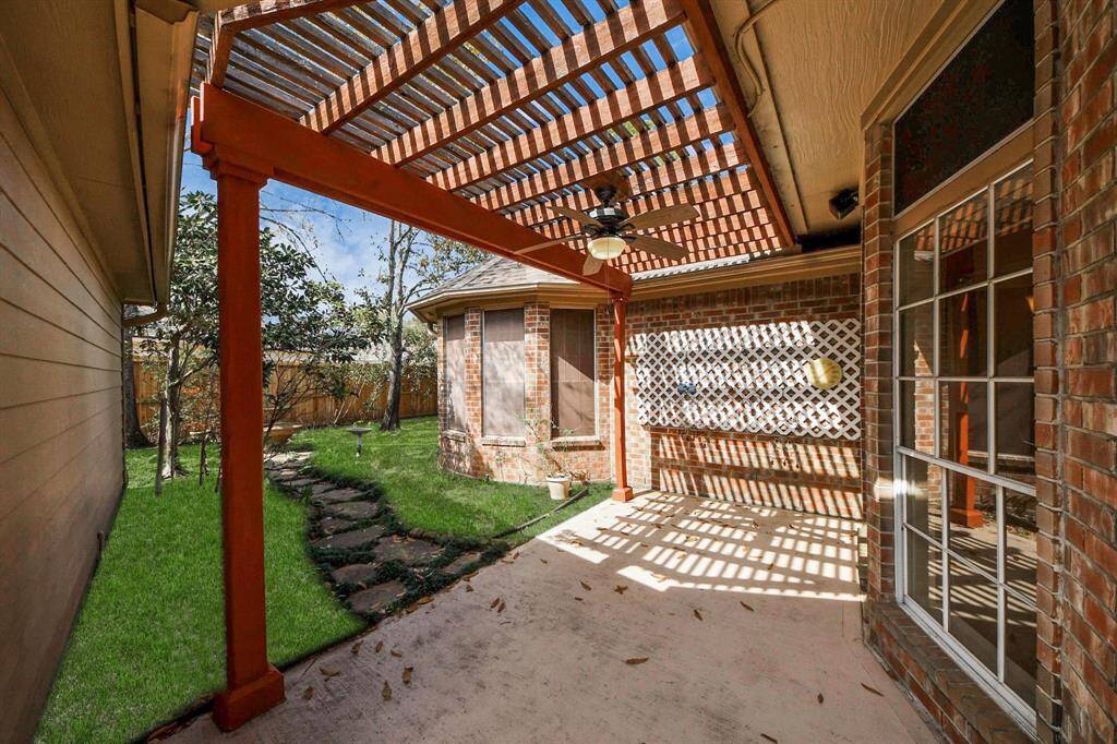 This photo showcases a charming patio area with a wooden pergola, brick walls, and a ceiling fan, providing a cozy outdoor space. The patio leads to a well-maintained garden with a stone path and lush greenery, making it ideal for relaxation and entertaining.