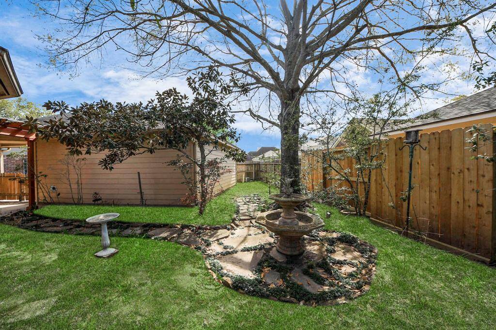 Charming backyard featuring a mature tree with a decorative stone path and central fountain. The space is enclosed by a wooden fence, offering privacy, and includes a small bird bath, creating a peaceful garden atmosphere.