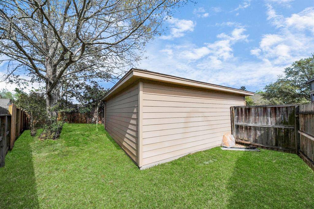 This photo shows a well-maintained backyard with a spacious lawn and mature tree, enclosed by a wooden fence. The area offers privacy and is ideal for outdoor activities or gardening.