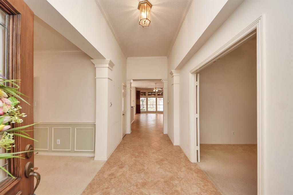 The photo shows a bright, welcoming entryway with a tiled floor, high ceiling, and elegant lighting. It leads to a spacious living area with large windows, offering a warm and inviting atmosphere.