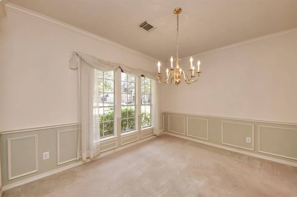 This room features elegant wainscoting and a classic chandelier, enhancing its traditional charm. Large windows with sheer curtains provide ample natural light, creating a bright and inviting space. Perfect for a dining area or formal living room.