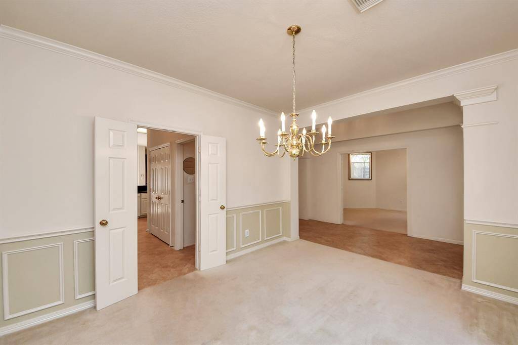 This photo showcases an elegant dining room featuring a classic chandelier, wainscoting, and neutral walls. The room connects to other areas through double doors and an open archway, offering a spacious and inviting atmosphere.