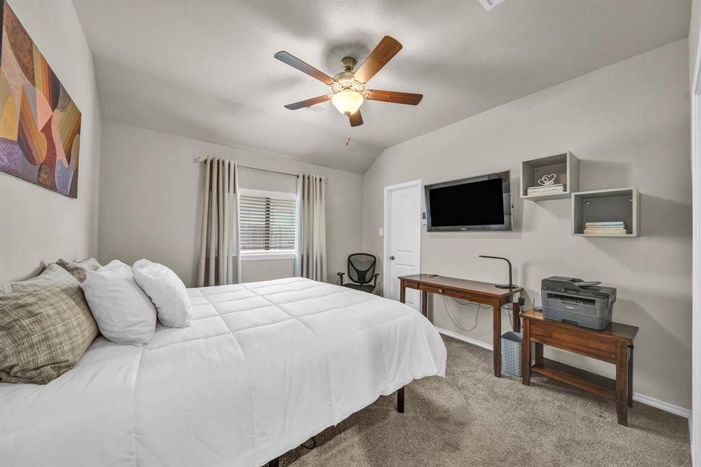 Guest bedroom with ceiling fan, workspace, and natural light.