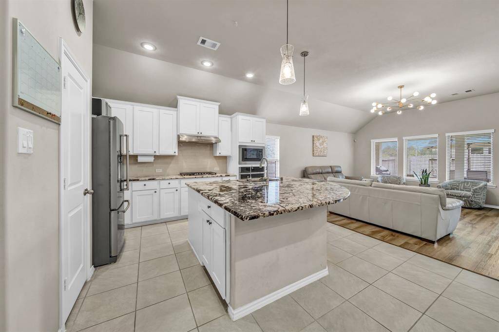 Open-concept kitchen and living area with island and granite countertops.
