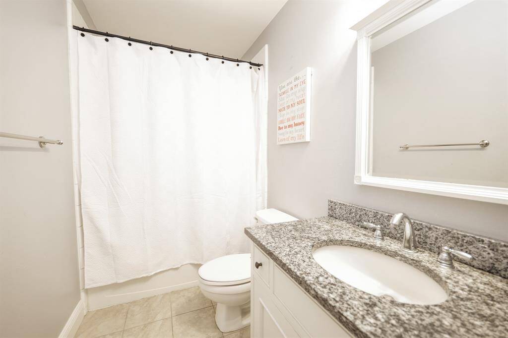 The secondary bathroom features a clean, functional layout with a combination tub and shower, modern fixtures, and ample storage which includes built-in shelves.