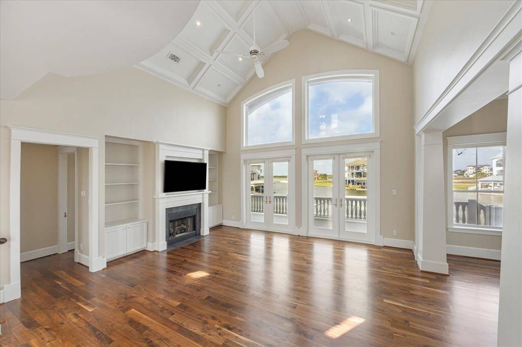 The expansive open living area features custom built-ins, a gas log fireplace, and striking polished plaster wall finishes, all beneath a paneled cathedral ceiling. A state-of-the-art home automation and audio-visual system enhances modern living