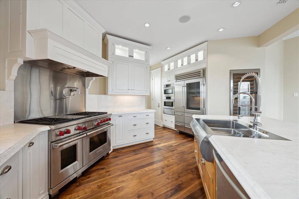 The gourmet kitchen is a culinary dream, featuring a Wolf 6 burner gas range with double oven, griddle & pot filler for convenience & a 96-bottle wine cooler. Rich wood floors complement the slab marble countertops and full-slab marble backsplash