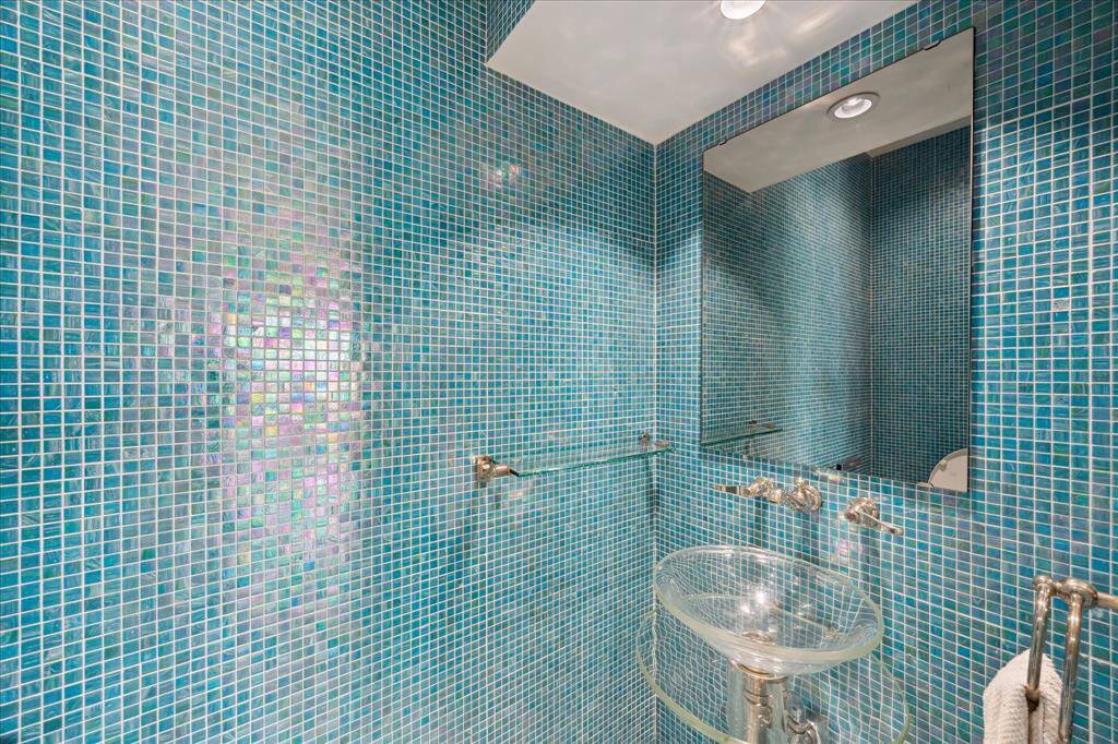 The jewel-box powder room features full-height handmade glass tile, a Lalique crystal faucet, glass pedestal sink, and a tankless bidet toilet with smart functions—an exquisite space that must be seen in person to truly appreciate