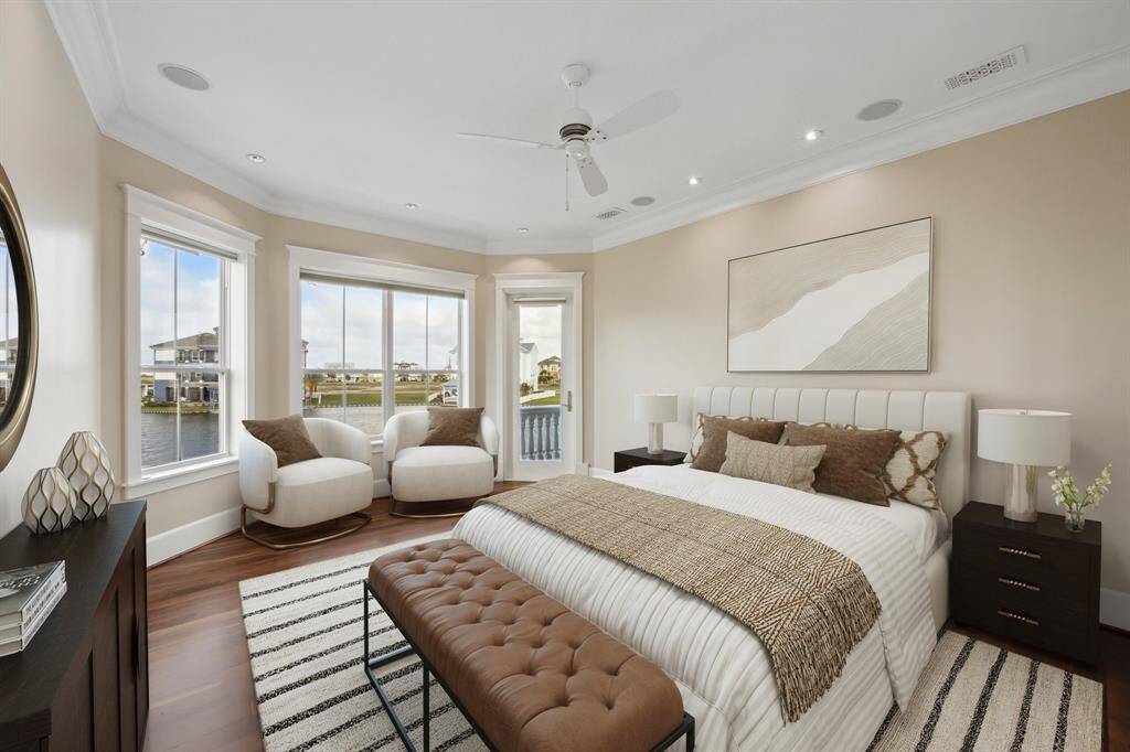 Private primary suite featuring a bay window with water views and direct access to a waterfront terrace. Includes a breakfast bar with refrigerator/freezer drawers and a built-in coffee maker, along with custom moldings, a detailed ceiling design, abundant natural light, and warm wood floors