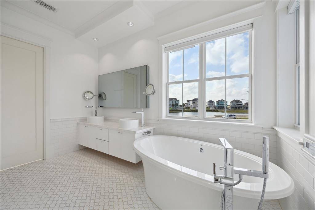 This spacious bath features an oversized air tub, dual vessel sinks, and abundant natural light from double windows and a side window near the closet. The mirror includes a built-in TV—just add a cable box for the ultimate in relaxation and convenience