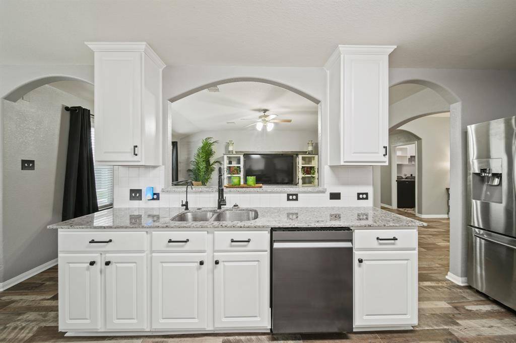 A double basin stainless steel under-mount sink sits just below an arched opening framed by upper cabinets overlooking the living room. Included is a kitchen sink water filtration system along with a whole home water softener installed in 2020.