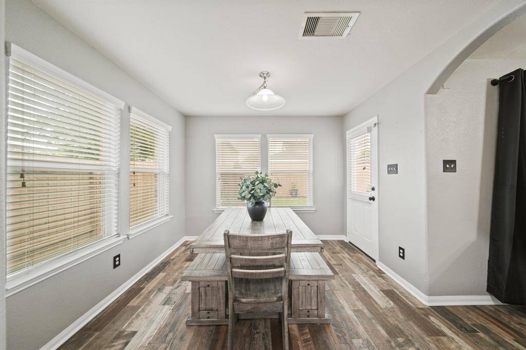 Surrounded by windows with blinds and a glass door leading to the patio & backyard is this bright cheery breakfast room with pendant chandelier lighting & hardwood tile flooring.