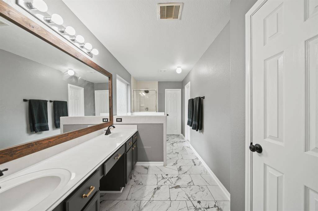 The bathroom includes painted cabinets supporting a solid surface counter top with integrated back splash and dual sinks accompanied by a wall mounted framed mirror with lighting above.