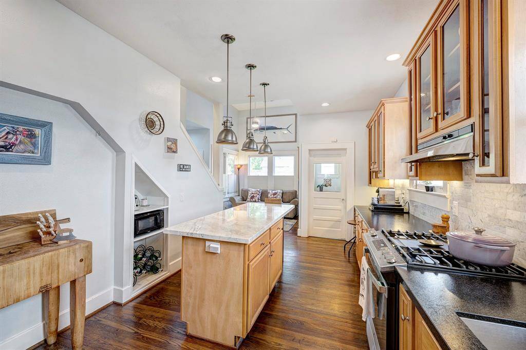 Gourmet kitchen offers honed granite counter, marble island, stainless steel appliances, marble tile backsplash, glass front cabinets and pendant lighting.