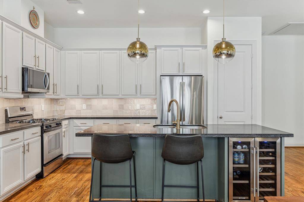 Modern kitchen featuring top-of-the-line appliances, including a 2024 LG stainless steel microwave, 2023 LG refrigerator, and an Orymuse wine fridge. The granite island with breakfast bar seating and Whirlpool gas range stove provide both style and functionality, complemented by a sleek stainless steel under-mount sink.
