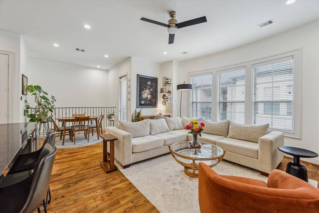This inviting second-floor living room features warm hardwood flooring and recessed LED lighting. The open layout connects seamlessly to the kitchen and breakfast room, creating a spacious and functional living area.
