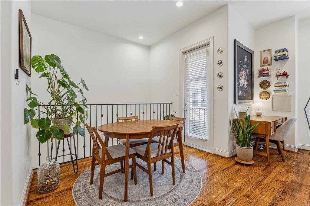 Bright and airy second-floor dining area featuring warm hardwood flooring, recessed LED lighting, matte black metal railing, and a door leading to the private balcony—perfect for morning coffee or evening relaxation.