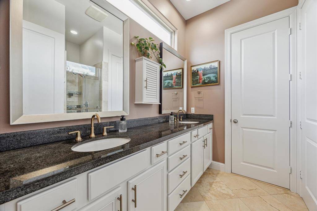 The primary bathroom features double under-mount sinks set in granite countertops, complemented by dual champagne bronze faucets and soft-close cabinetry for a polished, high-end look. Recessed LED lighting brightens the space, creating a clean and modern atmosphere.