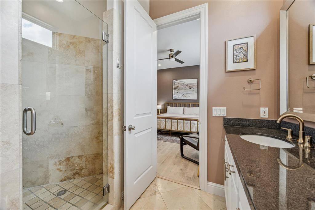 Relax in the walk-in shower, beautifully finished with travertine tile floors and walls for a spa-like feel. A sleek matte black ceiling fan adds a contemporary touch, completing this luxurious and functional retreat.