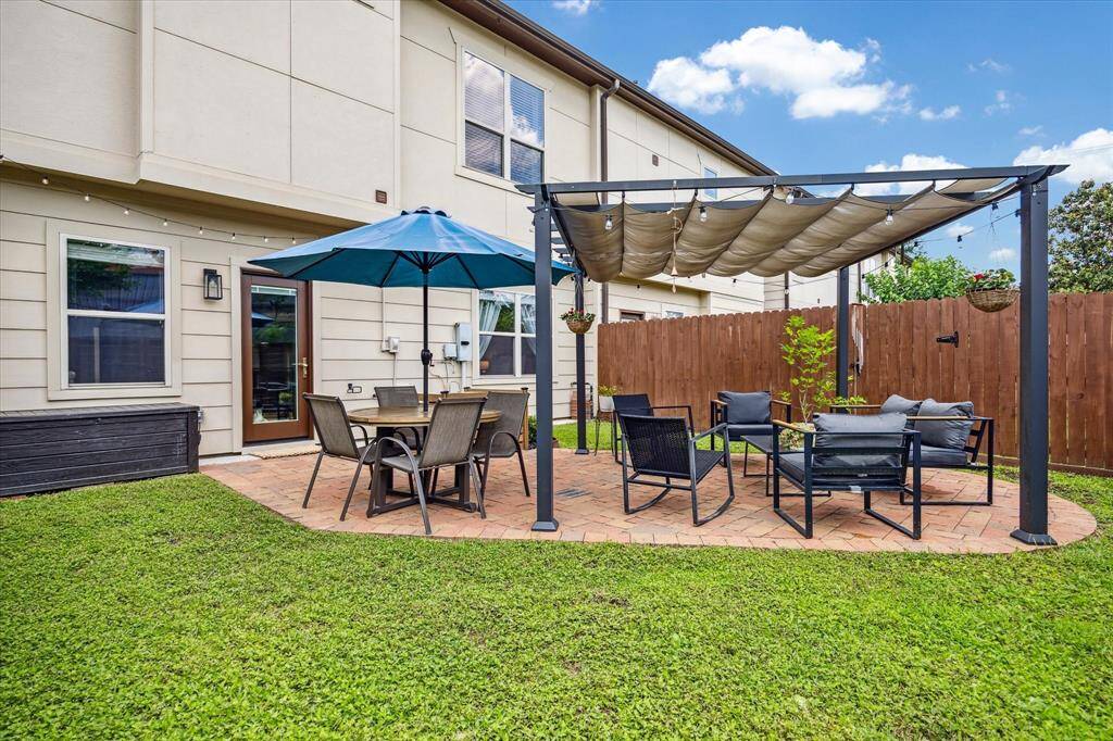 The backyard is a private oasis with lush landscaping and vibrant plants creating a serene atmosphere. A pergola-covered patio offers the perfect spot for outdoor dining or relaxation. Stained fencing adds warmth and privacy to this beautifully maintained outdoor space.