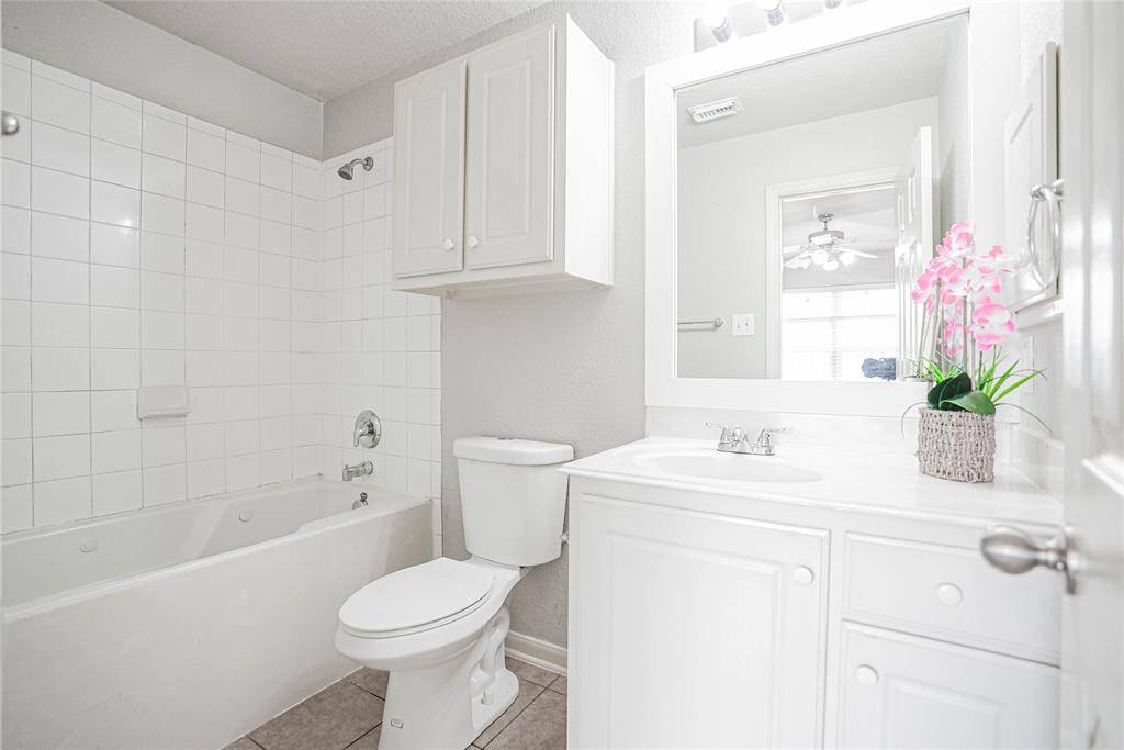 Bright and clean bathroom featuring a white vanity, bathtub with tiled walls, and ample storage. A large mirror enhances the space, and a touch of color is added with a floral arrangement.