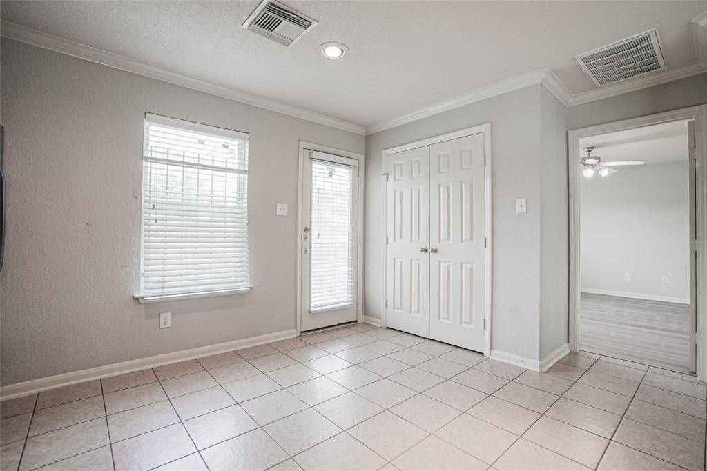 This bright room features tiled flooring, neutral walls, and ample natural light from a window and glass door. It includes a double-door closet and connects to an adjoining room with a ceiling fan.