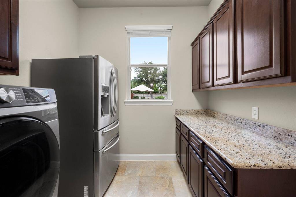 The spacious utility room offers plenty of room for an extra fridge or freezer, making it as functional as it is convenient. Built-in cabinetry with sleek granite countertops provides ample storage and folding space with a touch of style.