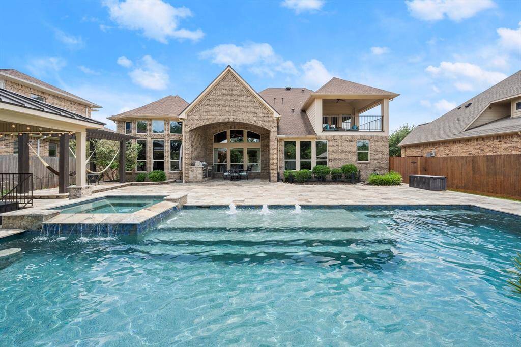 The Pebble Tec pool sparkles under the sun, featuring a built-in tanning shelf, bubblers, and waterfalls for ultimate resort-style relaxation.