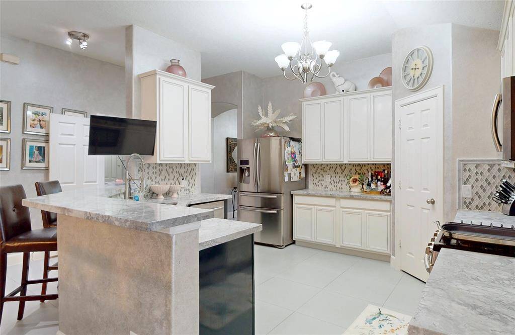This kitchen features modern appliances, abundant cabinetry, and a stylish backsplash. A large island with seating and elegant lighting enhance its functionality