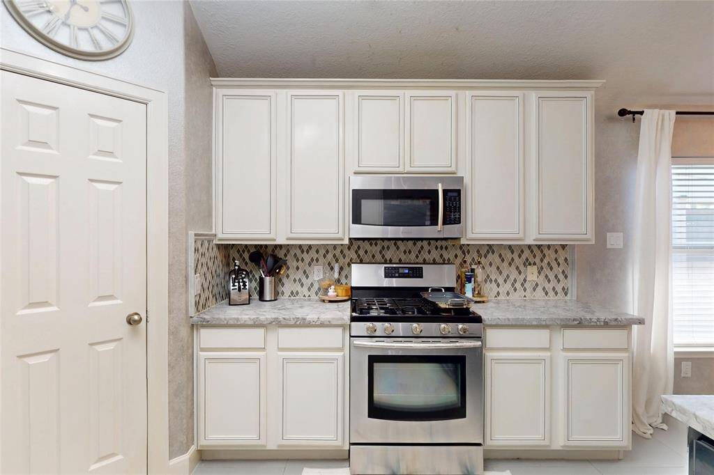 This kitchen features stainless steel appliances, a modern gas stove, and a built-in microwave. It has light cabinetry, a stylish tiled backsplash, and spacious counters, creating a bright and functional cooking area.
