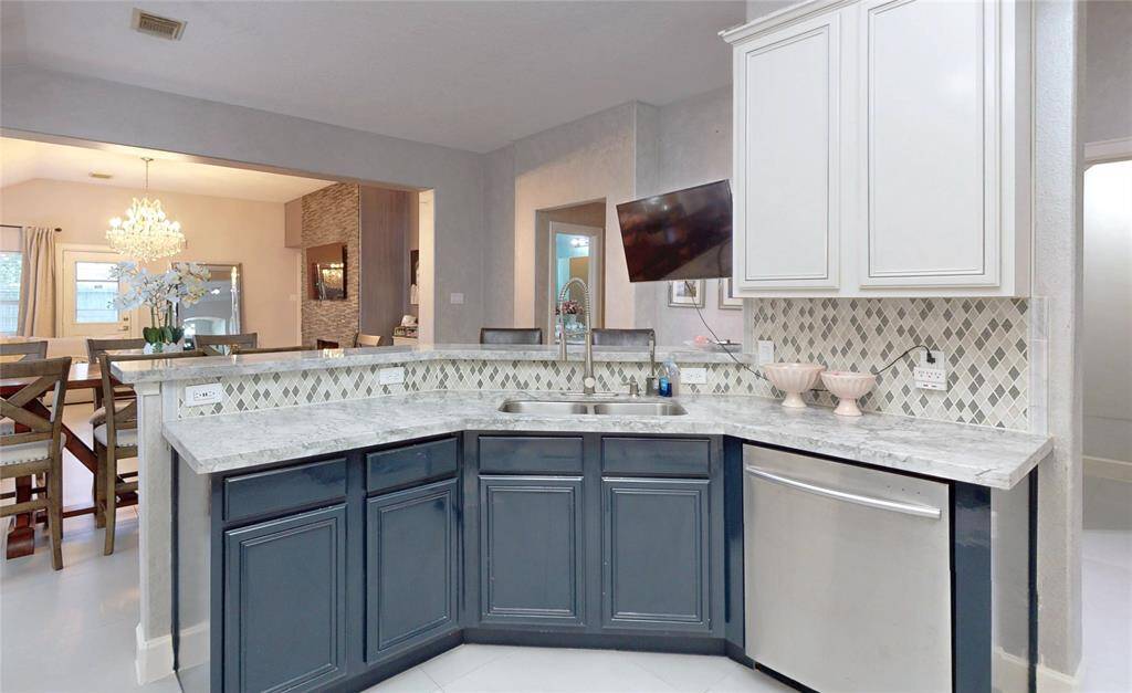 This kitchen features dual-tone cabinet scheme, combining white upper cabinets with dark lower cabinets. The marble countertops and diamond-patterned backsplash add elegance, while an open layout connects to a dining area with a chandelier, creating a spacious and inviting atmosphere.
