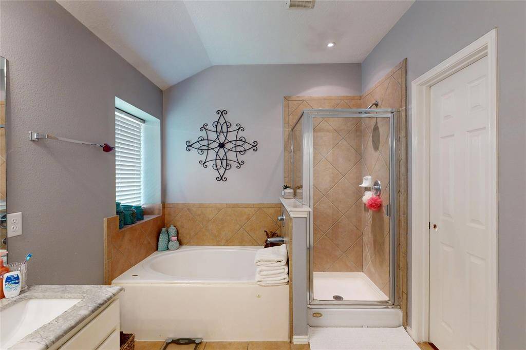 This bathroom features a modern design with a separate glass-enclosed shower and a cozy jetted bathtub. It has neutral-toned tiles, and natural light from a window with blinds.