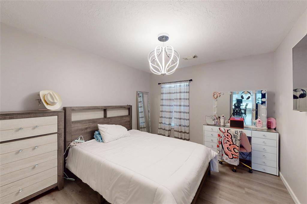 Cozy bedroom with modern lighting, neutral walls, and wood flooring. Natural light filters through striped curtains, creating a warm and inviting atmosphere.