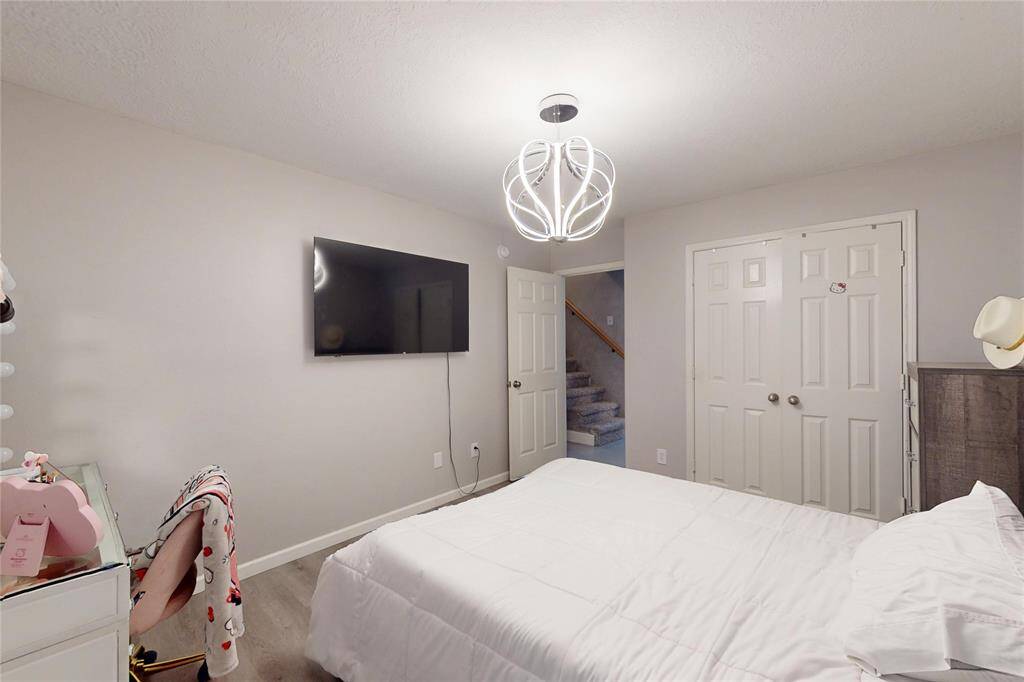 This bedroom features a modern light fixture, closet space with double doors. The room has neutral walls and flooring, providing a clean, contemporary look.