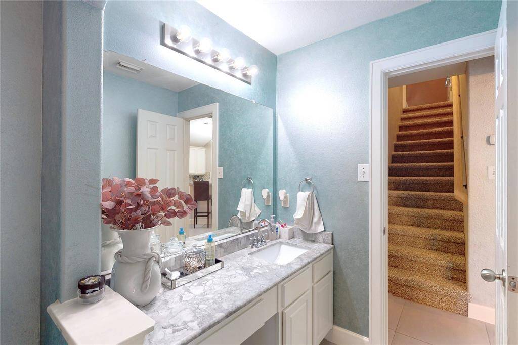 This photo showcases a modern bathroom with a marble countertop and stylish lighting. The walls are painted in a soothing soft teal color, and there's a staircase visible through an open door for multi-level access.