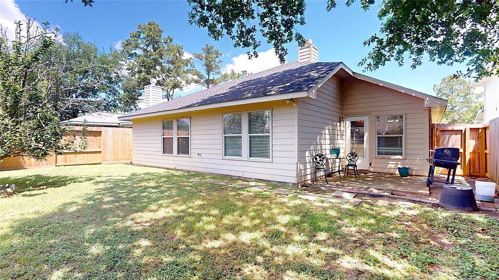 A cozy backyard with a charming patio area, ideal for outdoor relaxation. The house features a light-colored exterior, large windows, and a fenced yard that offers privacy. Perfect for enjoying sunny days.