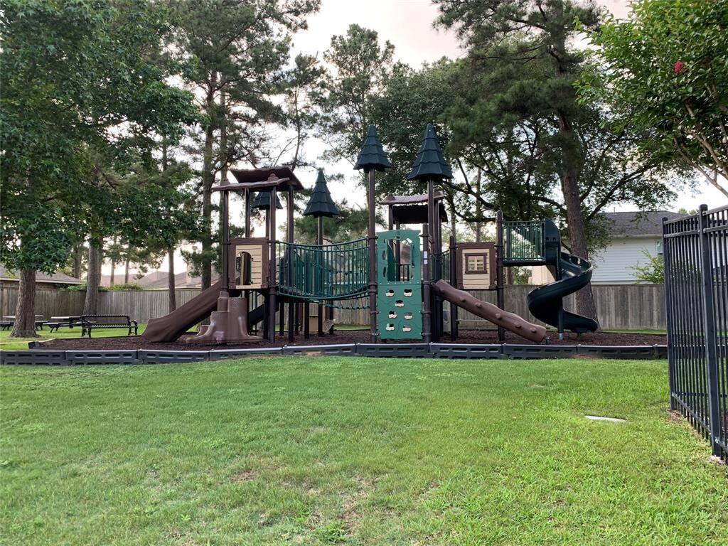 Across the street, a spacious, well-maintained playground with climbing structures and slides, surrounded by lush greenery and mature trees, ideal for families.