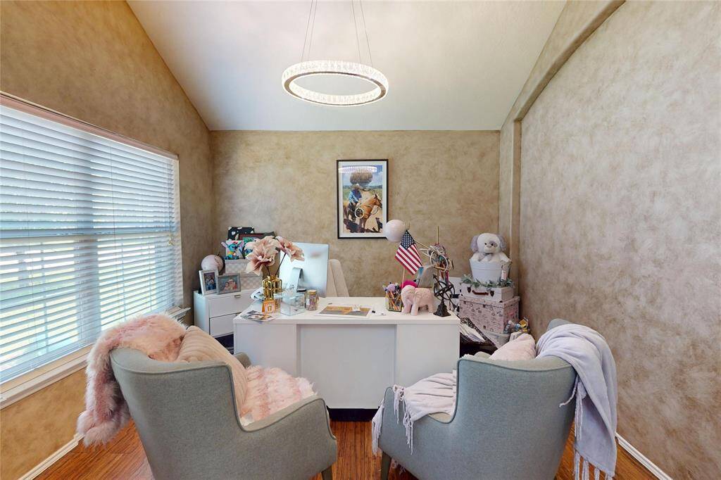 Charming home office with warm-toned walls, abundant natural light from a large window, and a sleek modern light fixture. Ideal for productivity, conveniently located off the entry hallway.